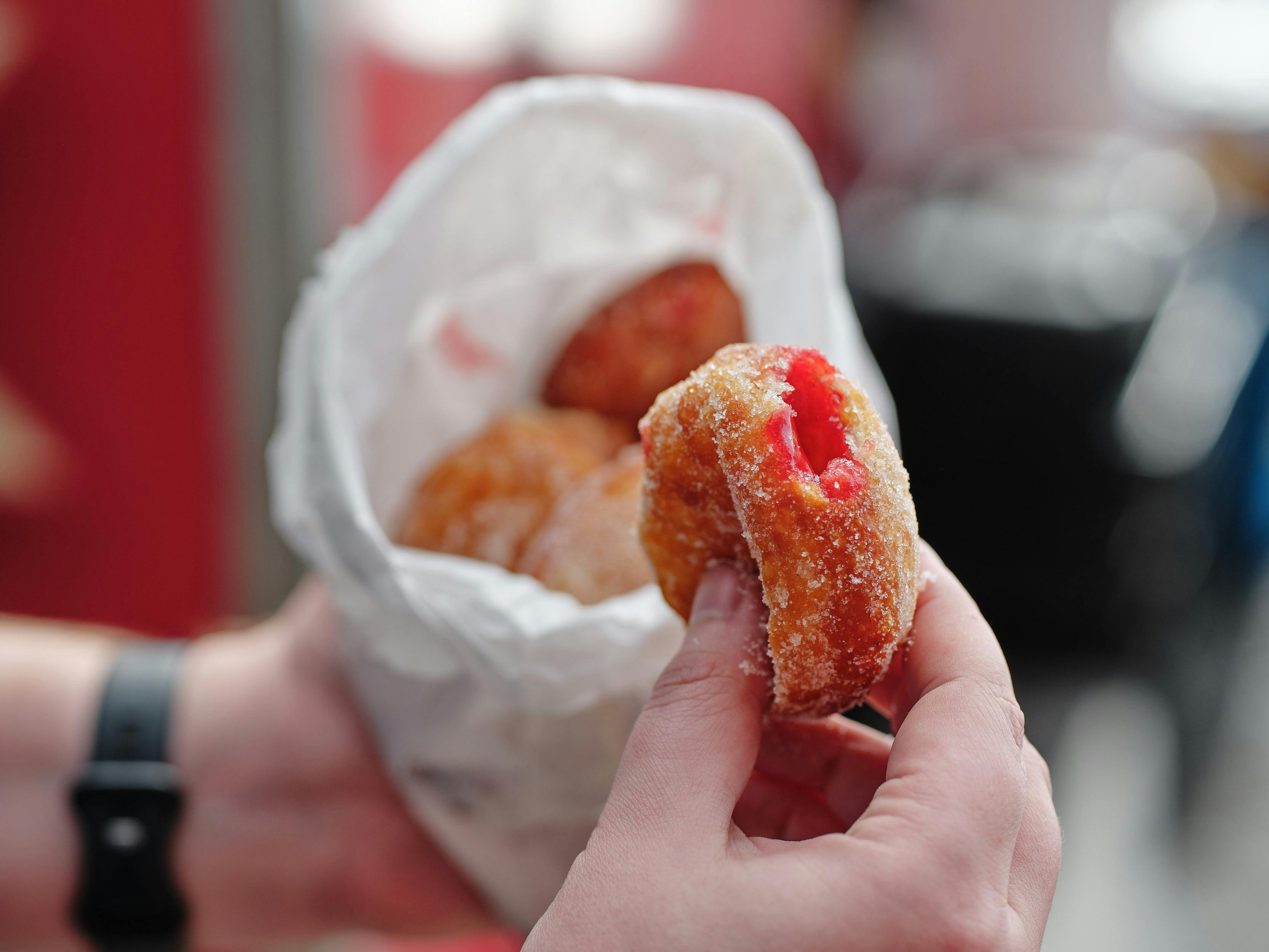 Fresh jam-filled doughnut dusted in sugar, held above a bag of doughnuts.