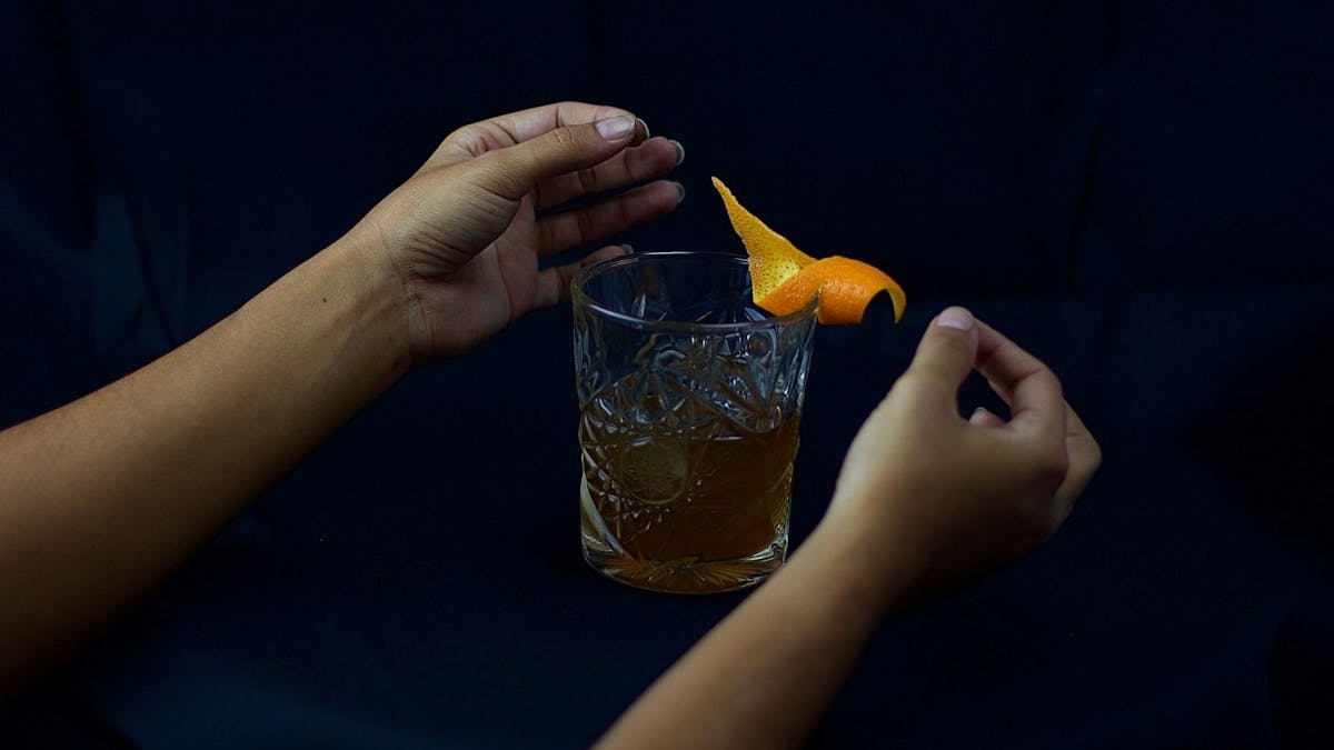 Old Fashioned Cocktail with hands placing orange twist garnish