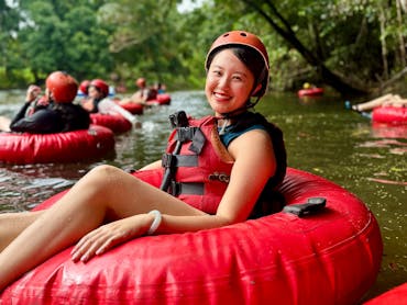 Woman in red tube and safety gear posed smiling at the camera as she floats down the Litlle Mulgrave