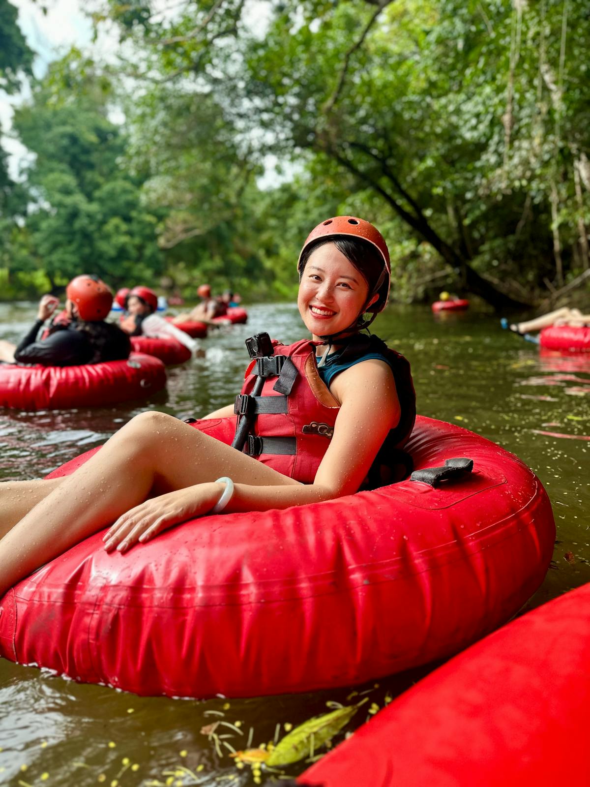 Woman in red tube and safety gear posed smiling at the camera as she floats down the Litlle Mulgrave