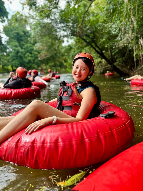 Woman in red tube and safety gear posed smiling at the camera as she floats down the Litlle Mulgrave