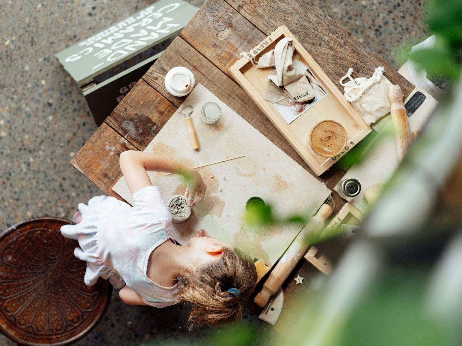 girl playing with clay on a wooden table with tools nearby
