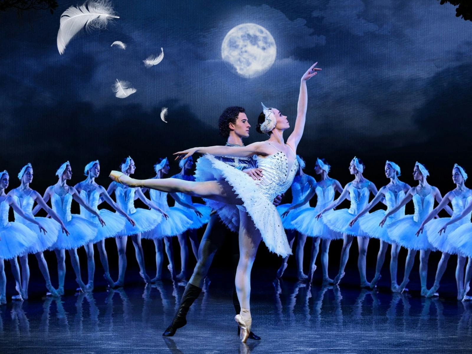 Ballet dancers perform Swan Lake on stage under a full moon, with the lead ballerina lifted by her.