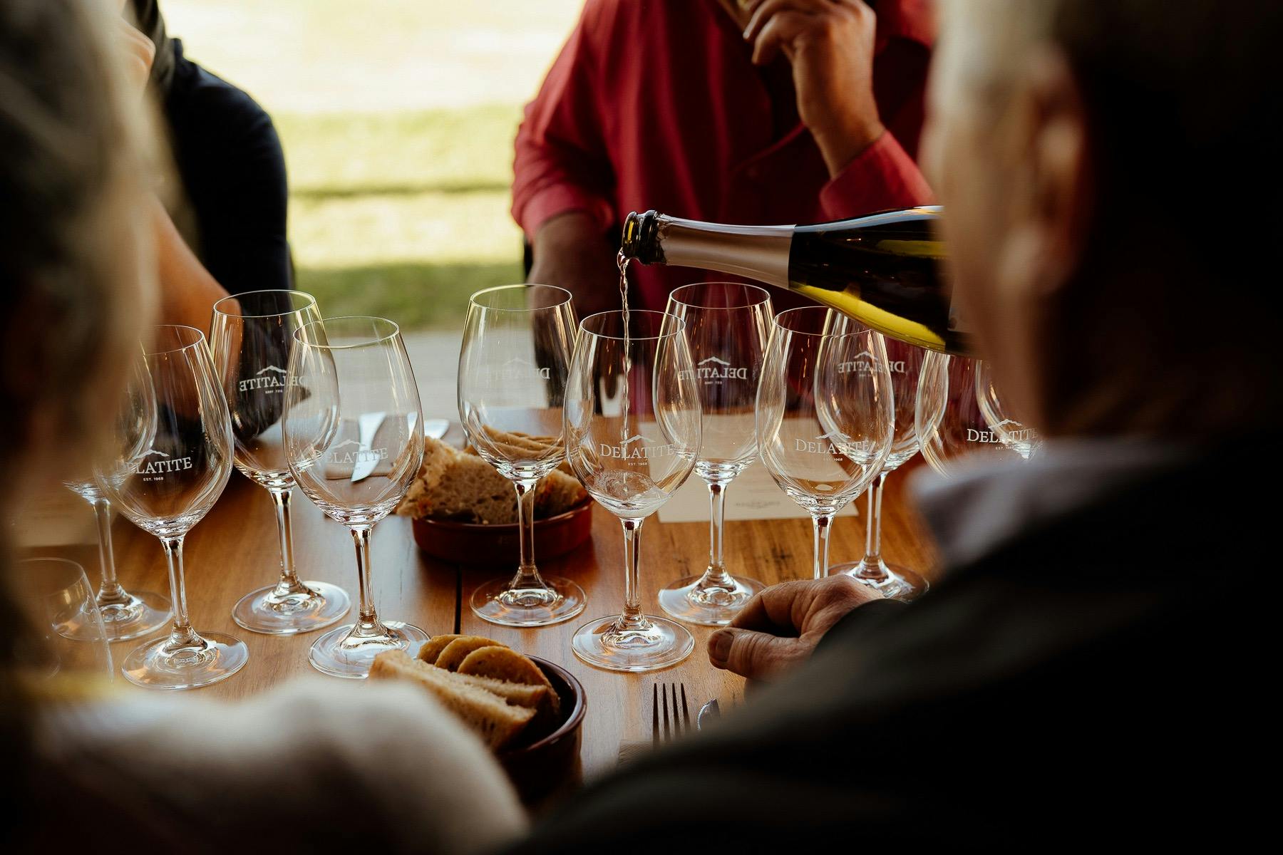 A bottle of wine being poured into a glass with four people framing the image
