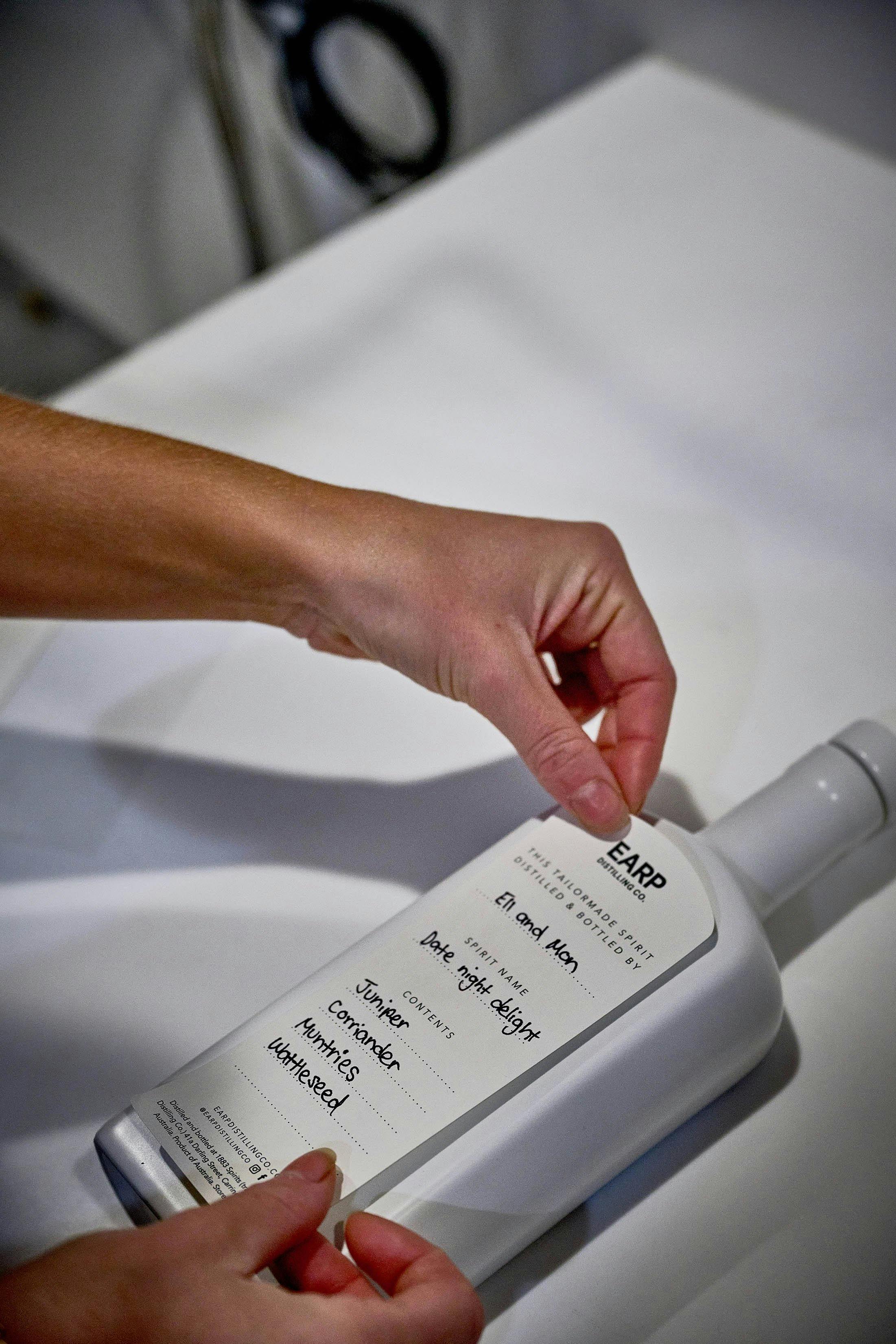 Hände legen sorgfältig handgeschriebenes Etikett auf weiße Flasche