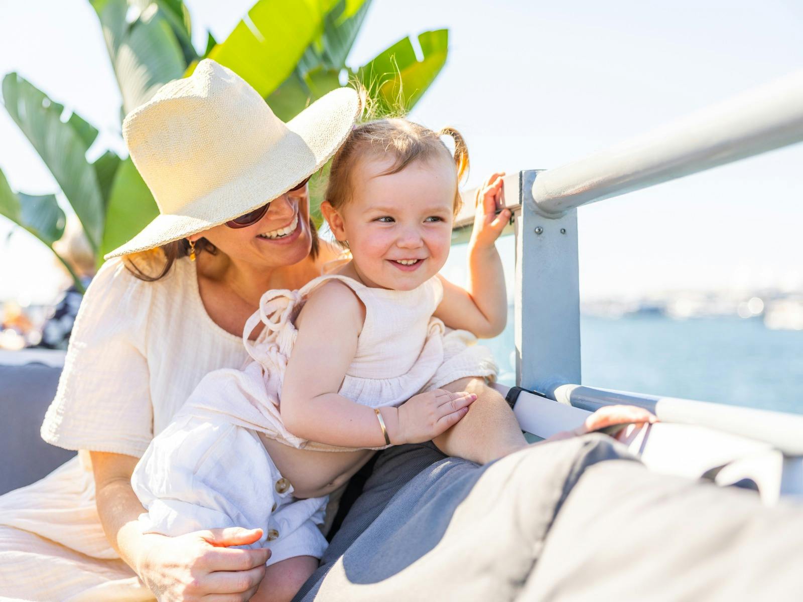 Mother in a wide brim sun hat having fun with her 18 month old daughter.