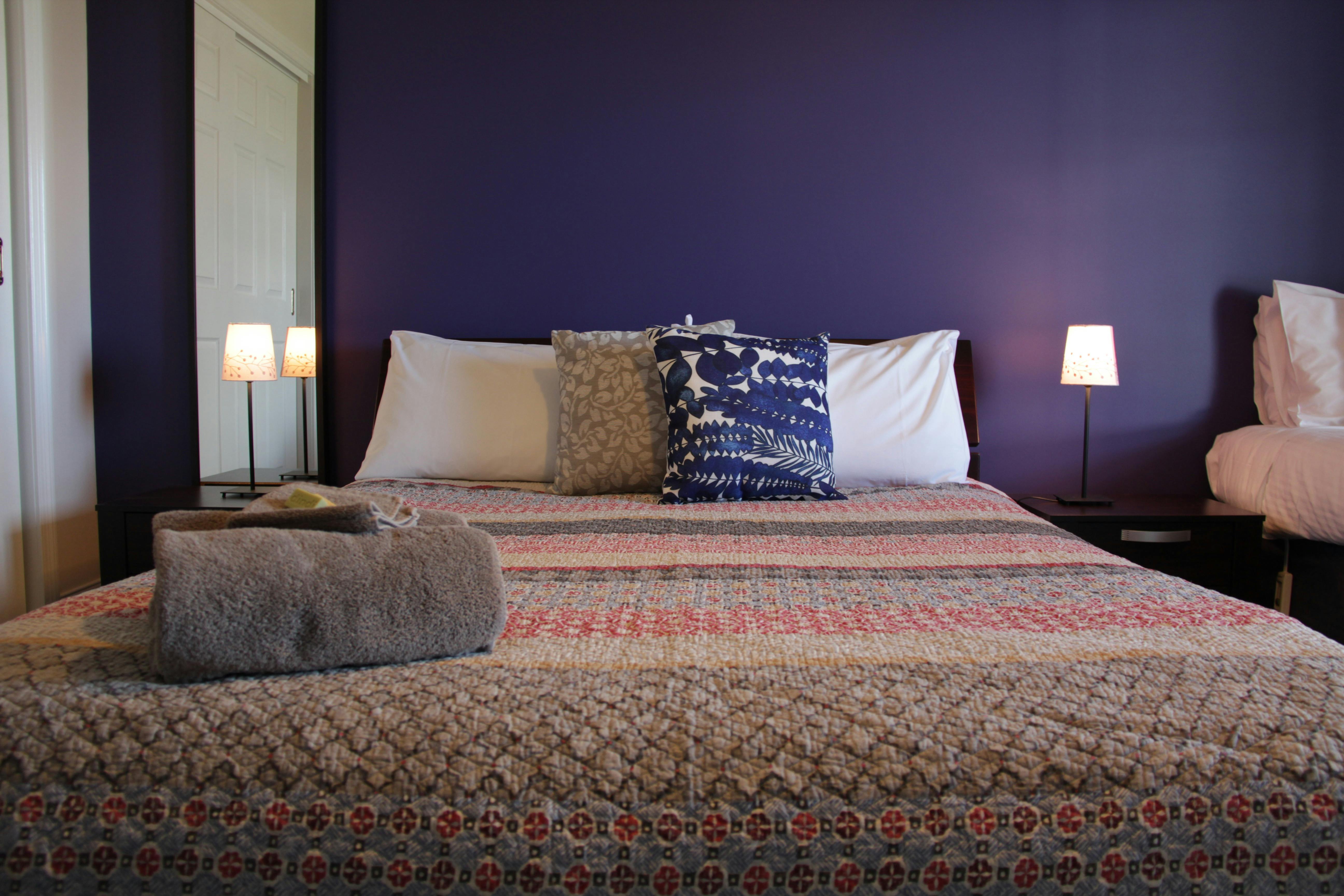 Queen size bed and a single bed in a room with a purple wall