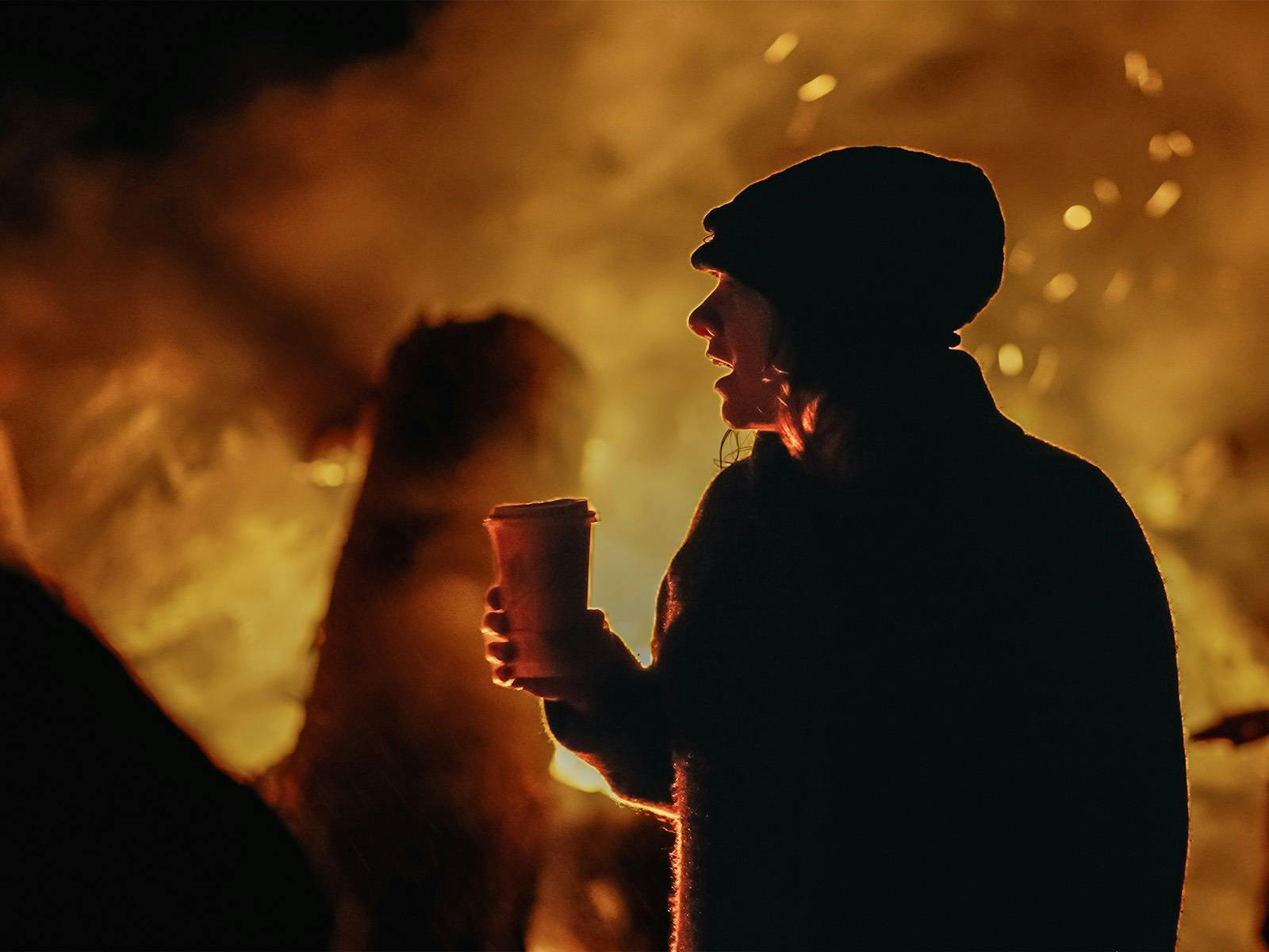 A sillouette of of a woman with embers and glow of a fire behind her.