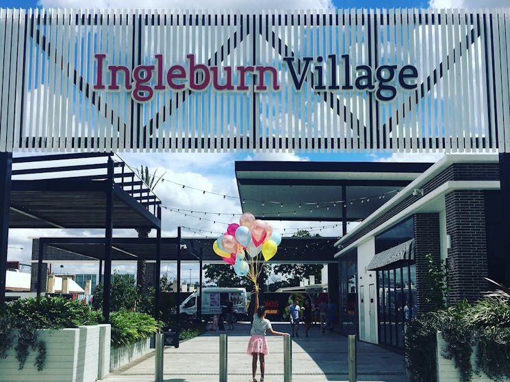 Girl standing with balloons in front of Ingleburn Village sign