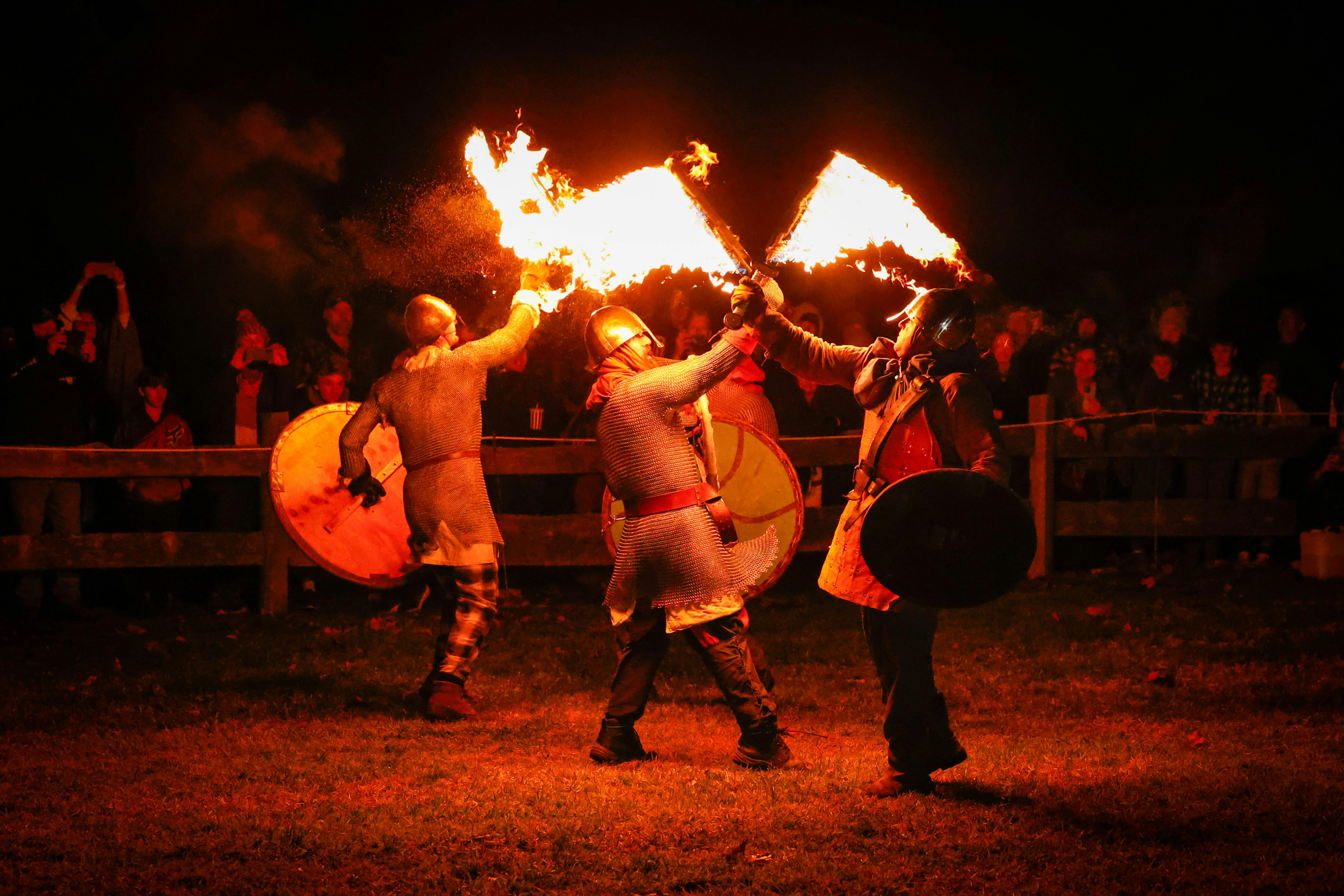 Four people in medieval costumes fight with flaming swords at night