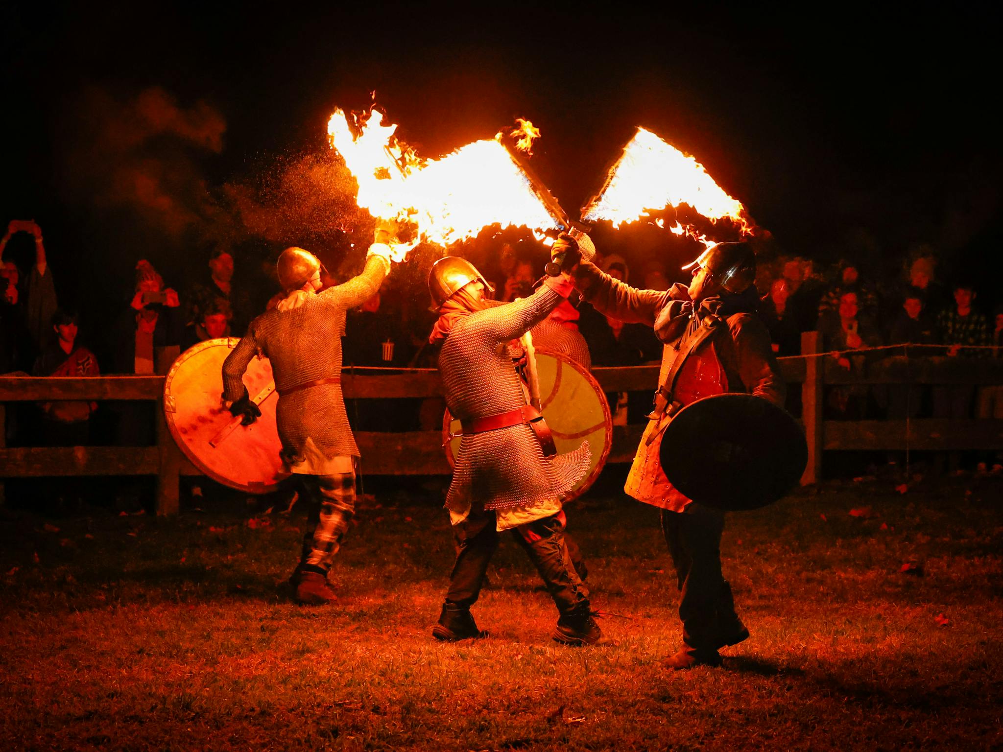 Four people in medieval costumes fight with flaming swords at night