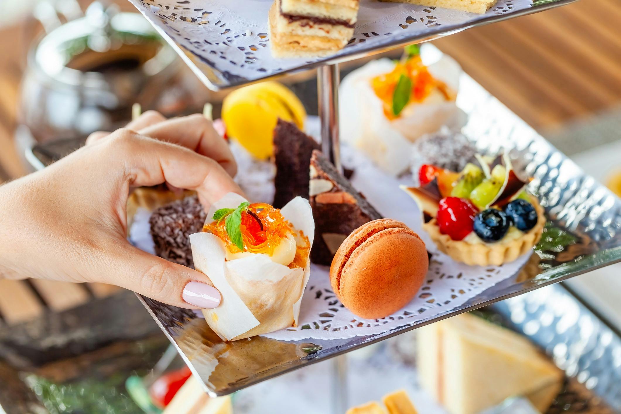 Hand holding a small canape from a high tea stand.
