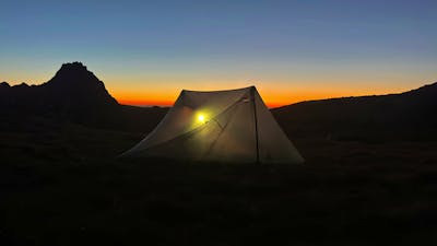 A tent in the mountains as the sun sets.