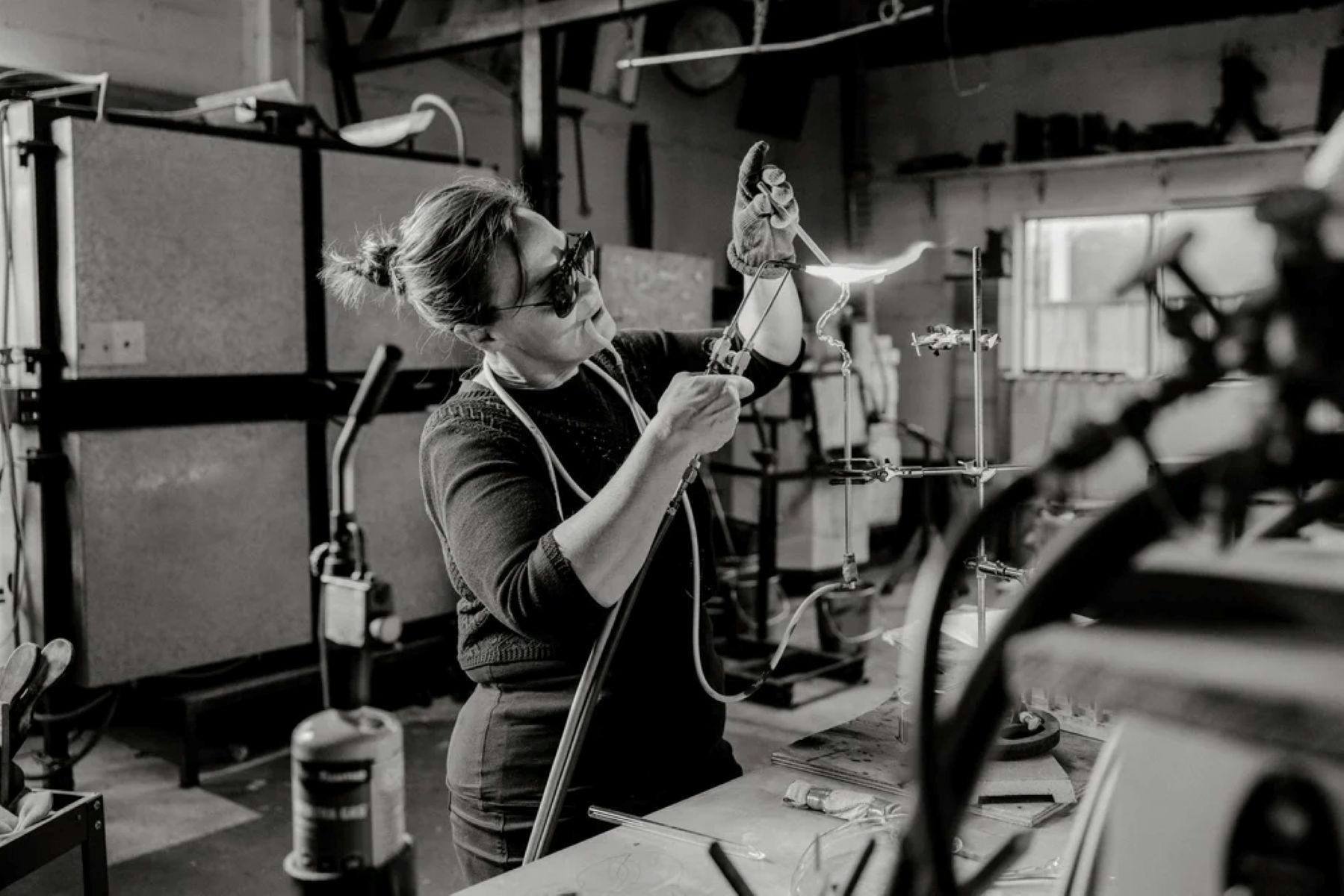 A black and white photograph of the artist with a blow torch  creating glass art