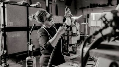 A black and white photograph of the artist with a blow torch creating glass art