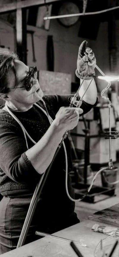 A black and white photograph of the artist with a blow torch creating glass art