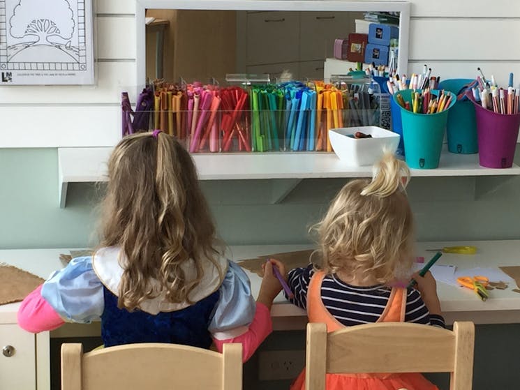 Two girls are sitting at a table drawing