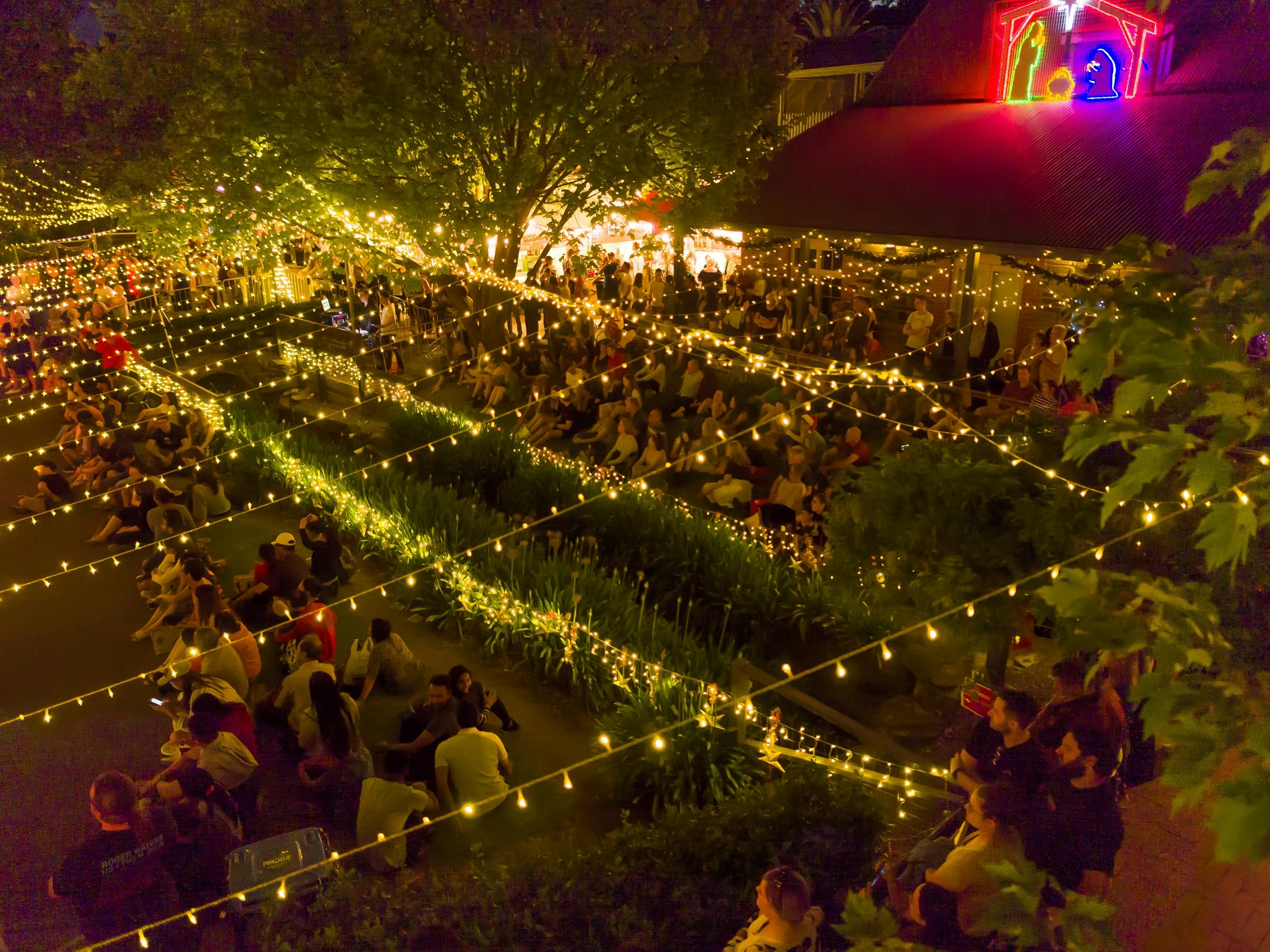 Overhead shot of market. View of fairy lights overhead the crowd watching the Carols.