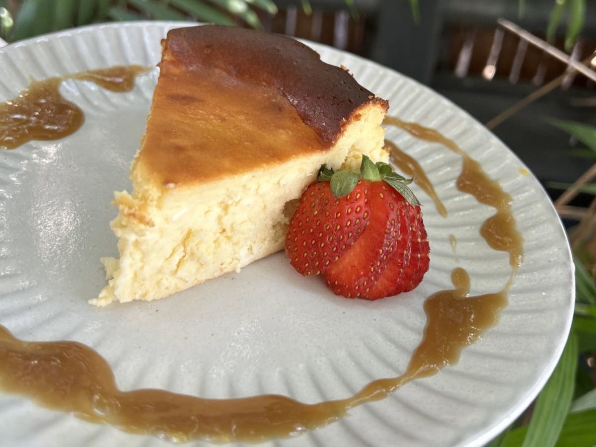 Baked cheesecake served on a white plate with a halved fresh strawberry and drizzled caramel sauce