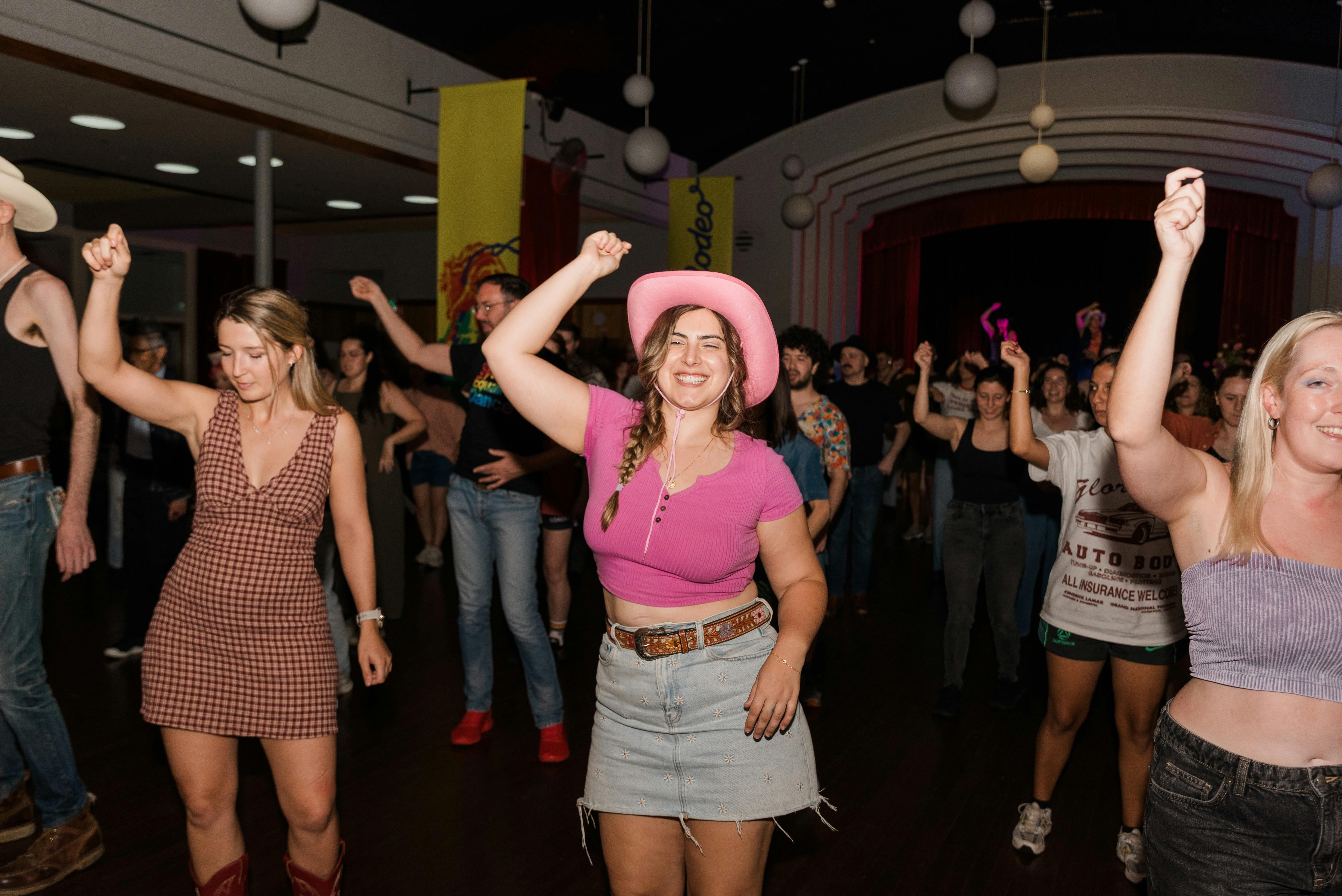 A person in a pink crop top and pink cowgirl hat makes a lasoo motion with their arm.
