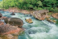 Wide shot of a rafting boat surrounded by blue water, lush rainforest and large boulders in Tully