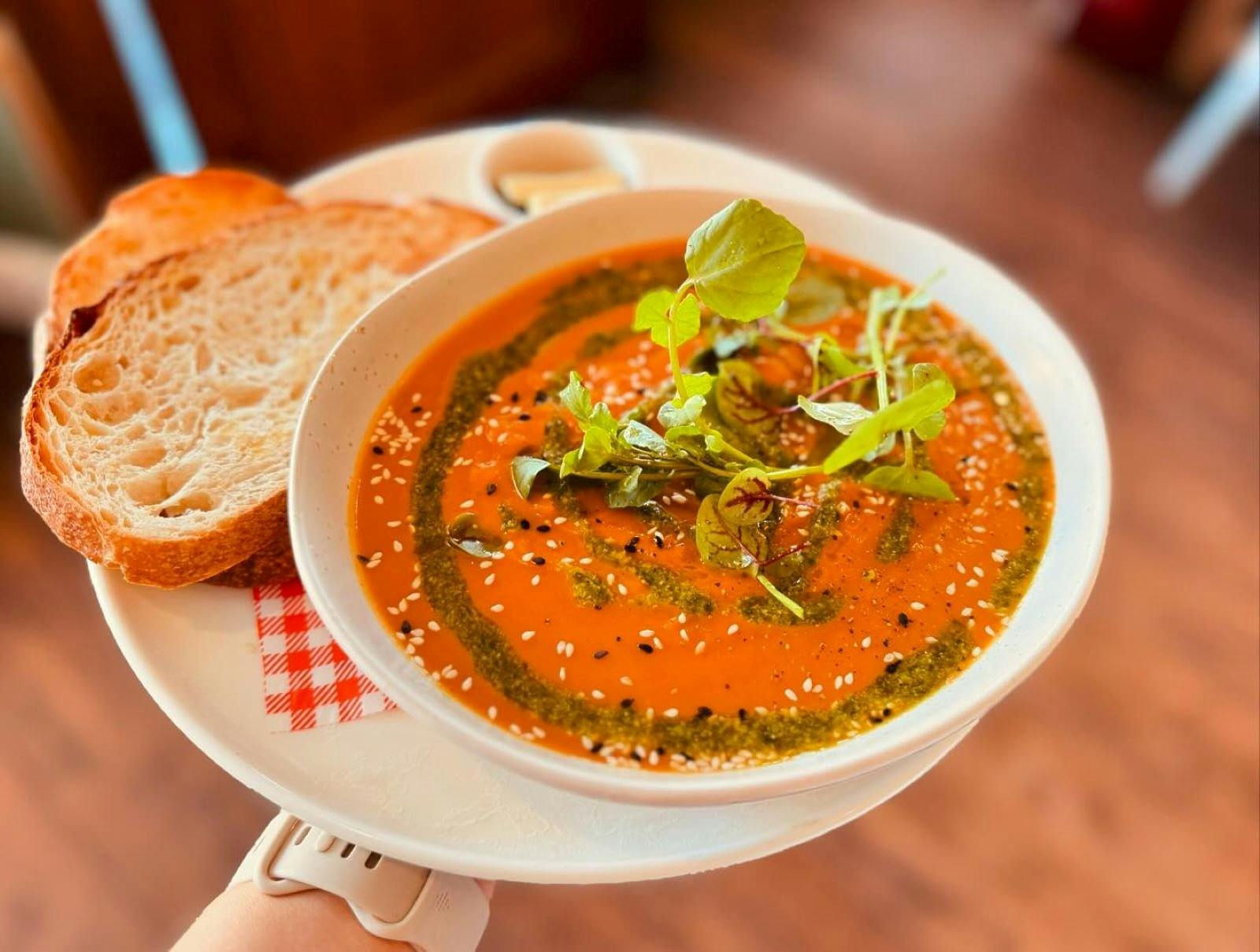 A bright bowl of sweet potato + pumpkin soup with a drizzle of pesto. Served with sourdough bread.