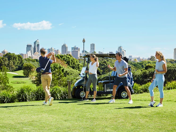 Four people teeing off with Sydney's city skyline in the background