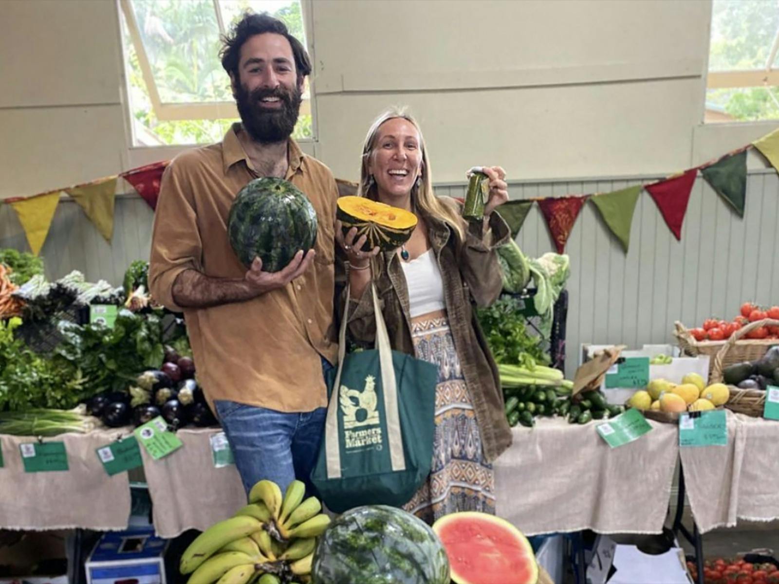 Two market customers holding up organic produce