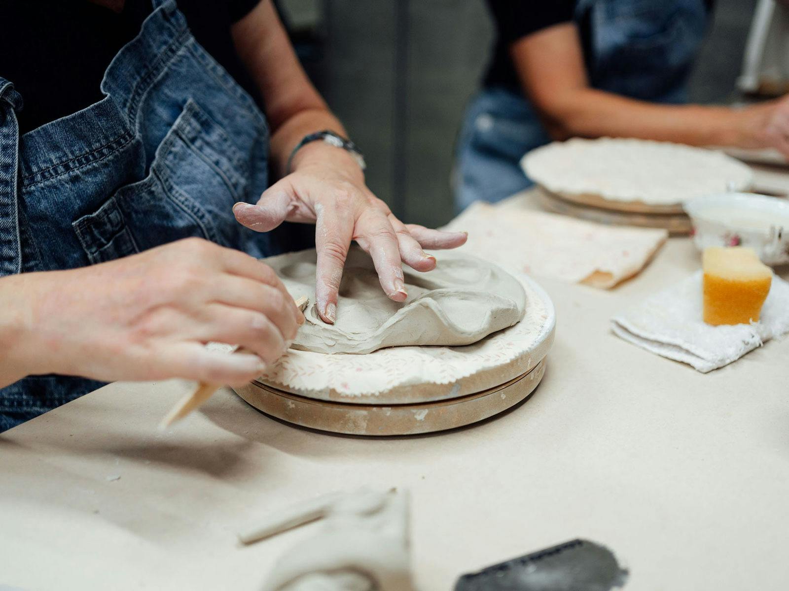 person shaping clay on a manual wheel