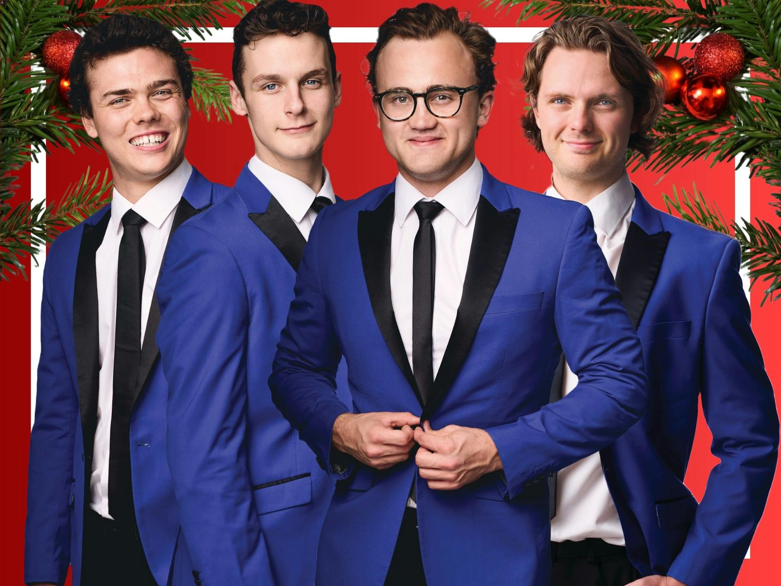 Four men in blue suits with festive backdrop, smiling confidently for a holiday-themed photo.