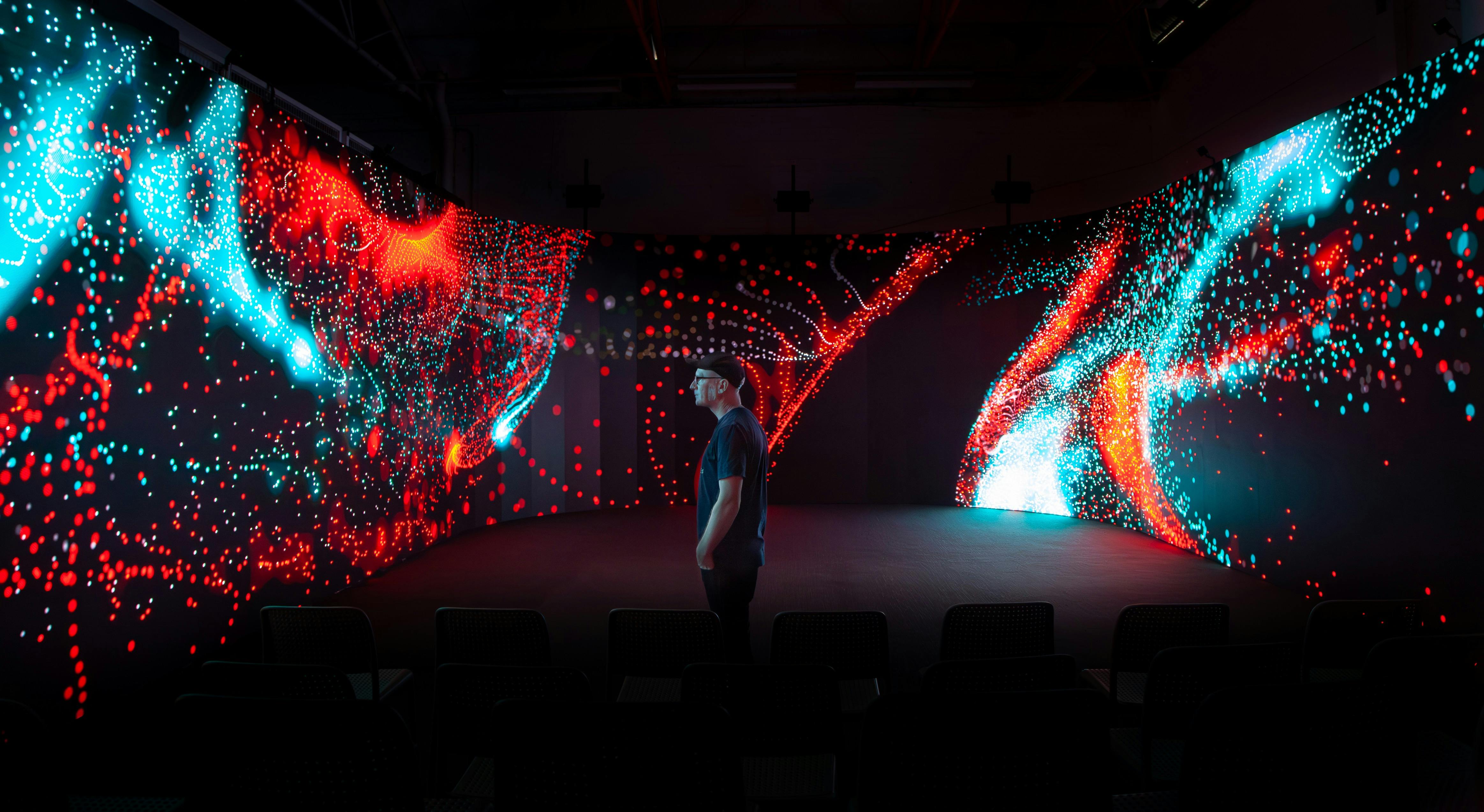 A man standing next to 150sqm of LED screens with an abstract digital artwork show.