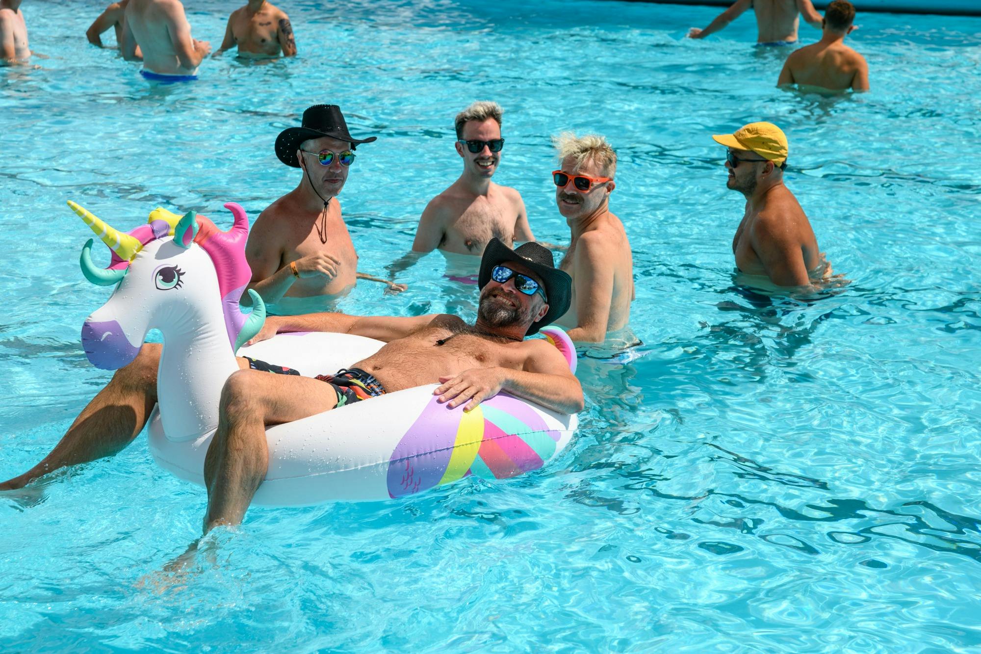 festival-goer sits in blow up unicorn floatie in outdoor swimming pool as four others look on