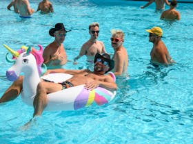 festival-goer sits in blow up unicorn floatie in outdoor swimming pool as four others look on