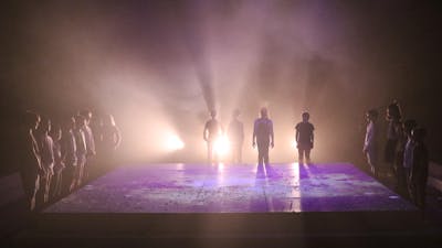 16 silhouettes of children standing around an elevated rectangle square that is backlit