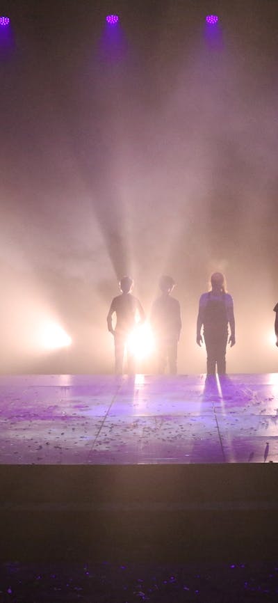 16 silhouettes of children standing around an elevated rectangle square that is backlit