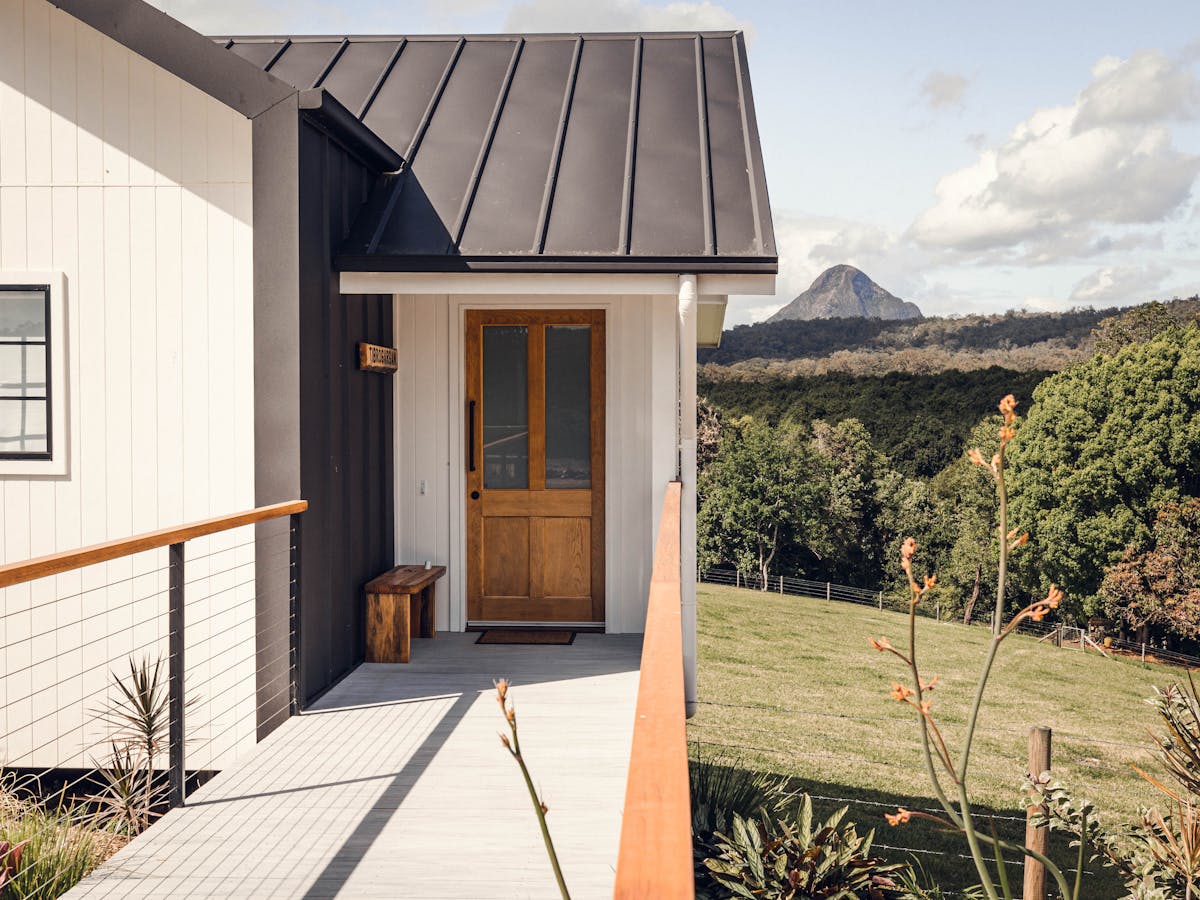 Walkway to entrance door of your cabin with a view of the cow paddock and Glasshouse Mountain behind
