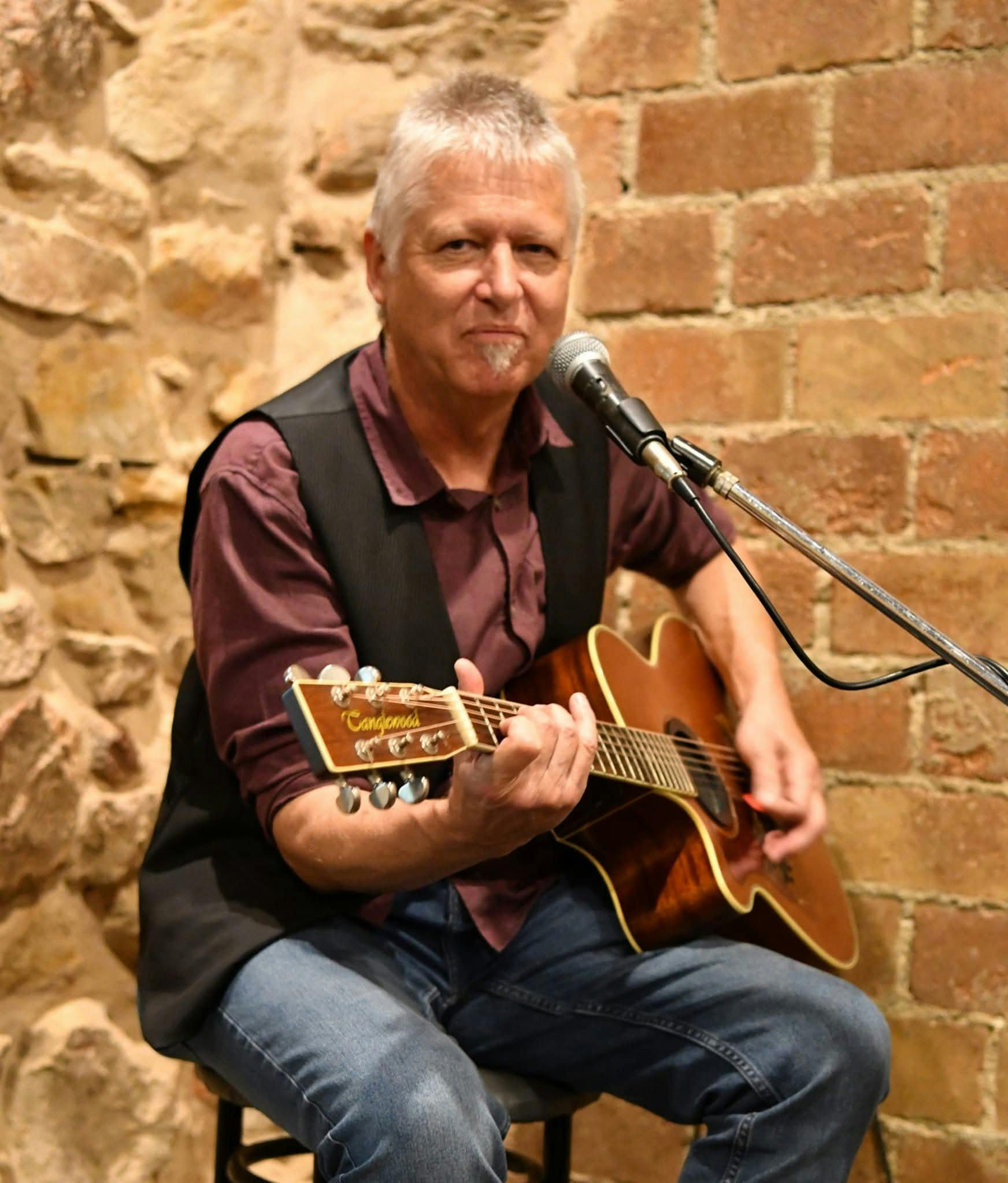 Mick Kidd sitting on a stool playing guitar