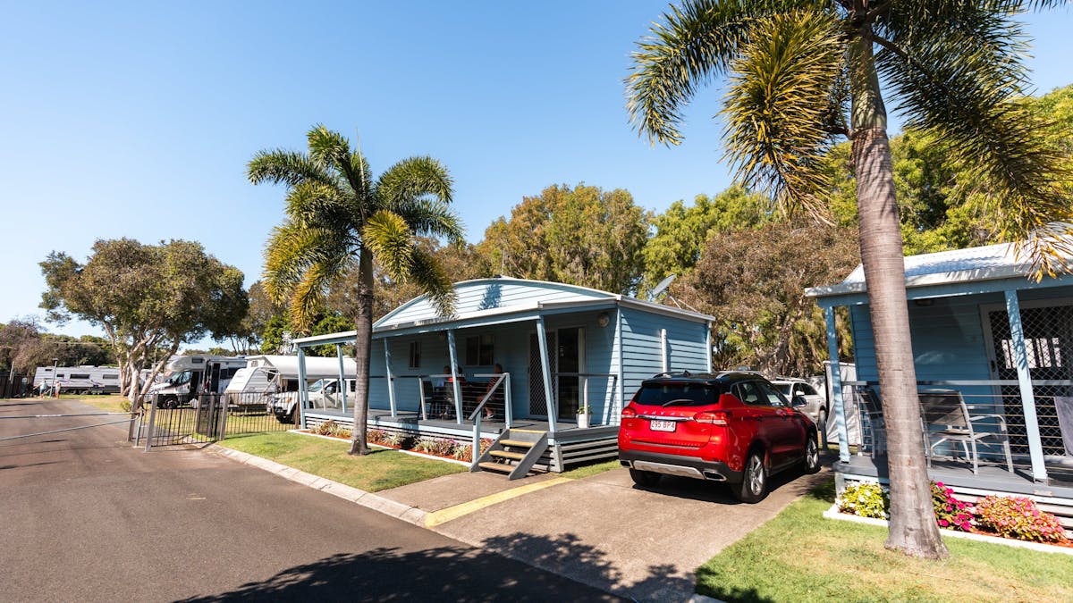 Shot of Mudjimba Beach Holiday Park cabin with palm trees and red car in small drive way