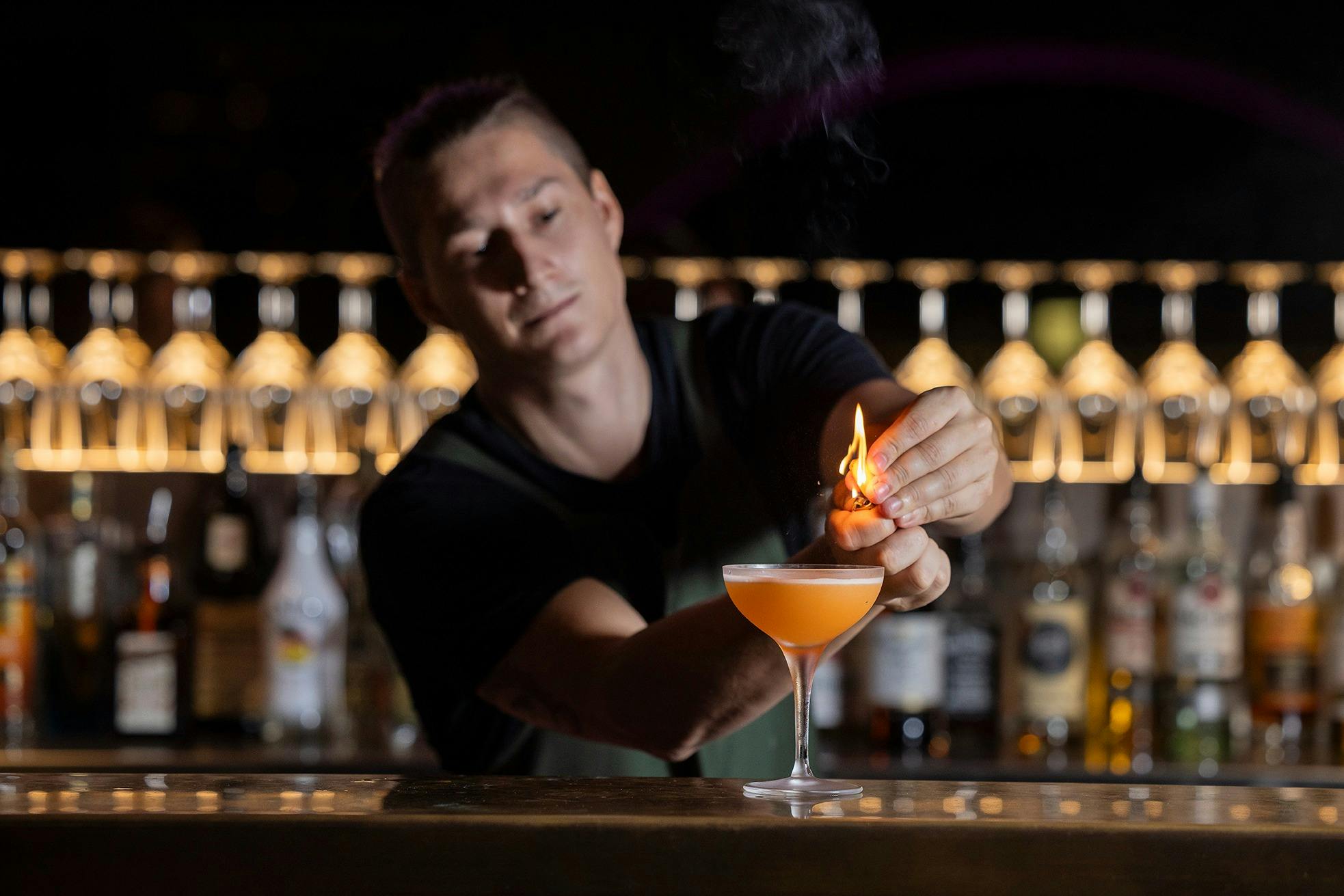 A bartender at the bar lights a flame above a signature 74 Islands cocktail