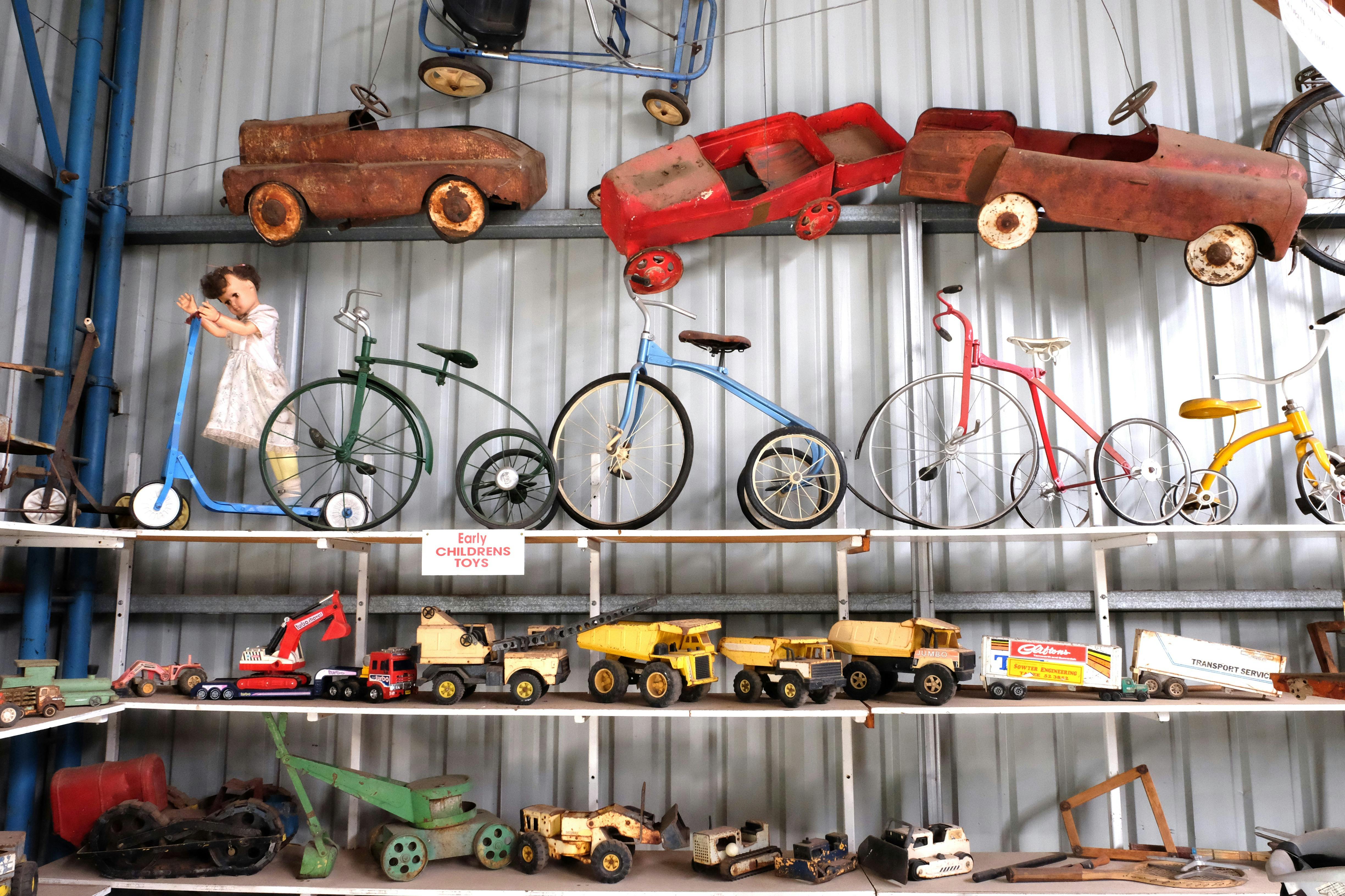silver wall with three shelves filled with push bikes, push carts and sandpit toys