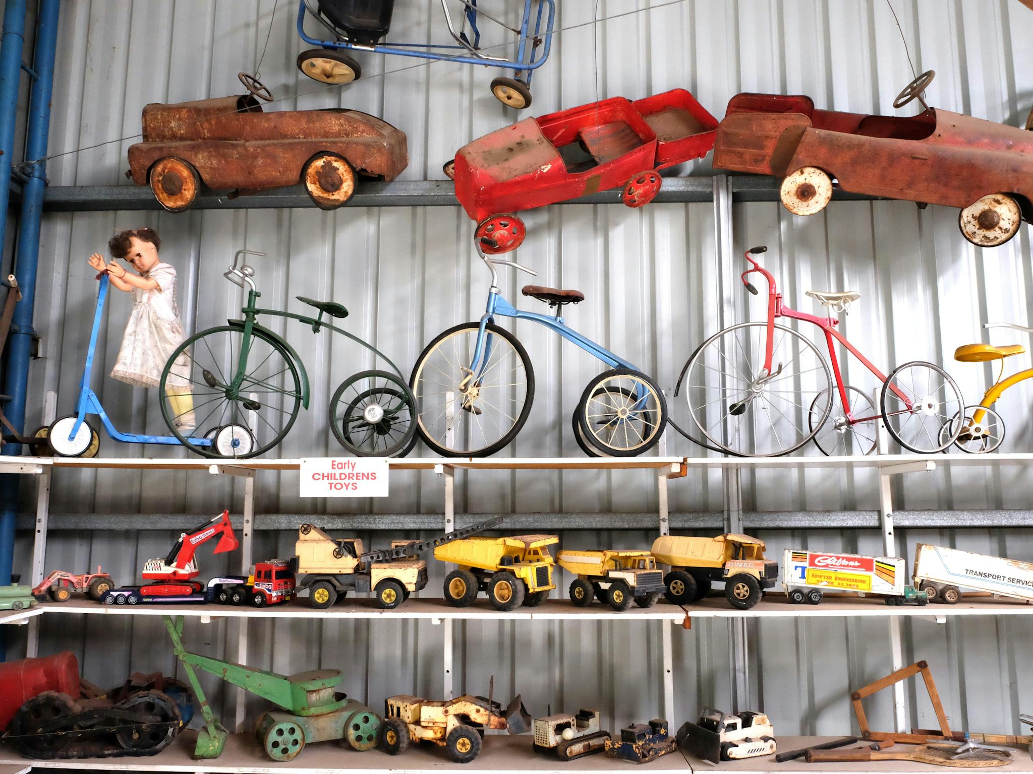 silver wall with three shelves filled with push bikes, push carts and sandpit toys