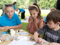 Smiling nanny doing craft to two young children in a park
