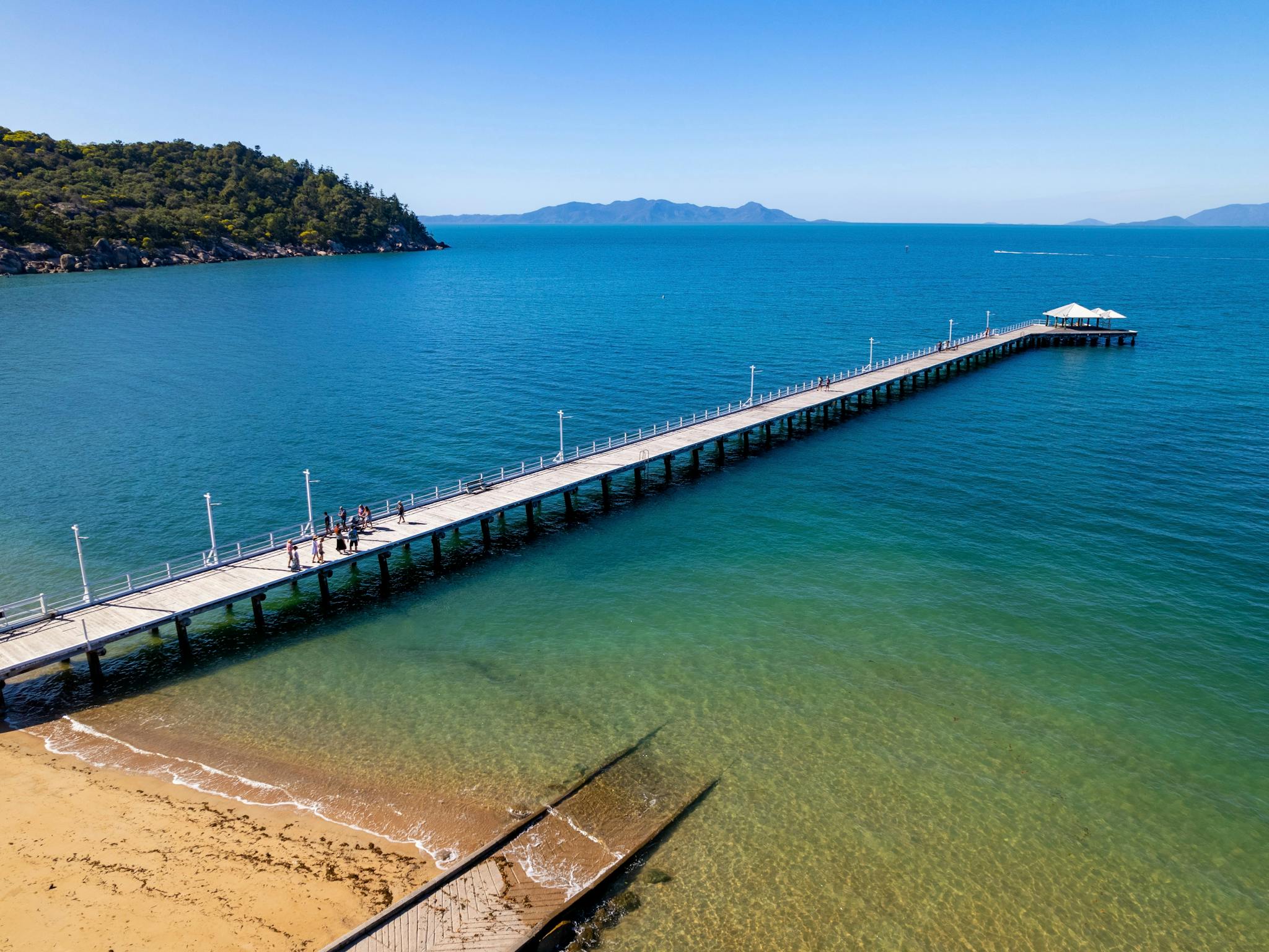 drone shot of tour group walking along a jetty with tree covered hills behind drone shot of tour group walking along a jetty with tree covered hills behind