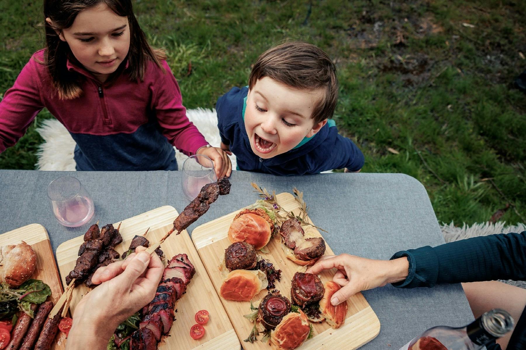 Wooden boards with assorted meats and two children eating