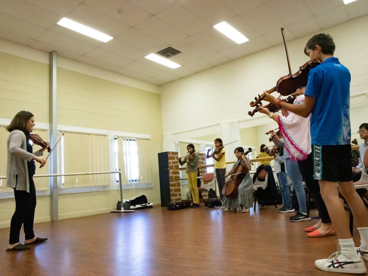 A group of string players receive encouraging guidance from a musician A group of string players receive encouraging guidance from a musician