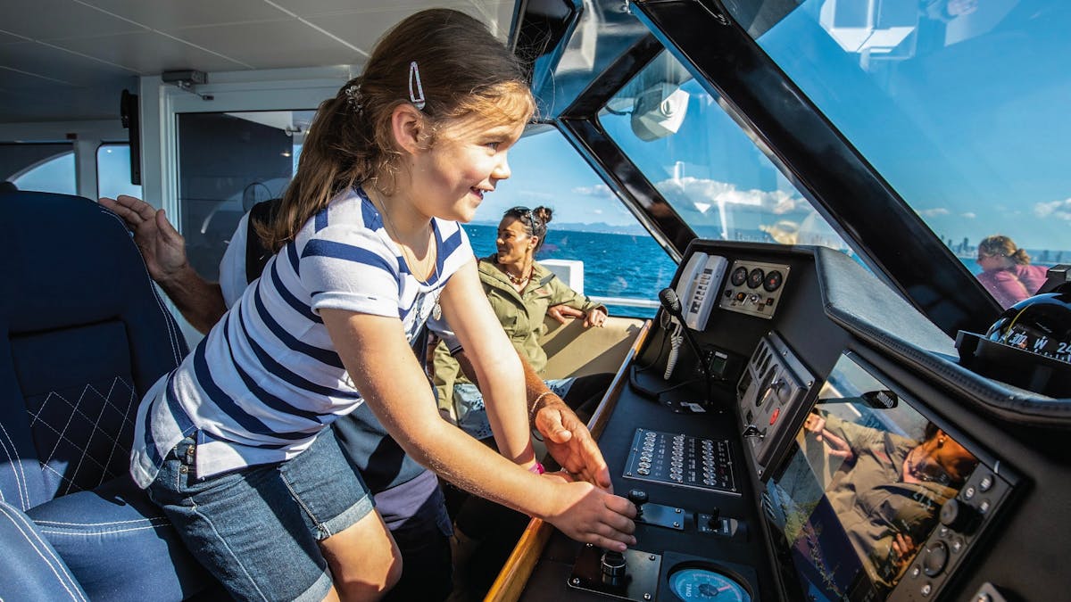 Excited young girl at helm of boat next to boat skipper