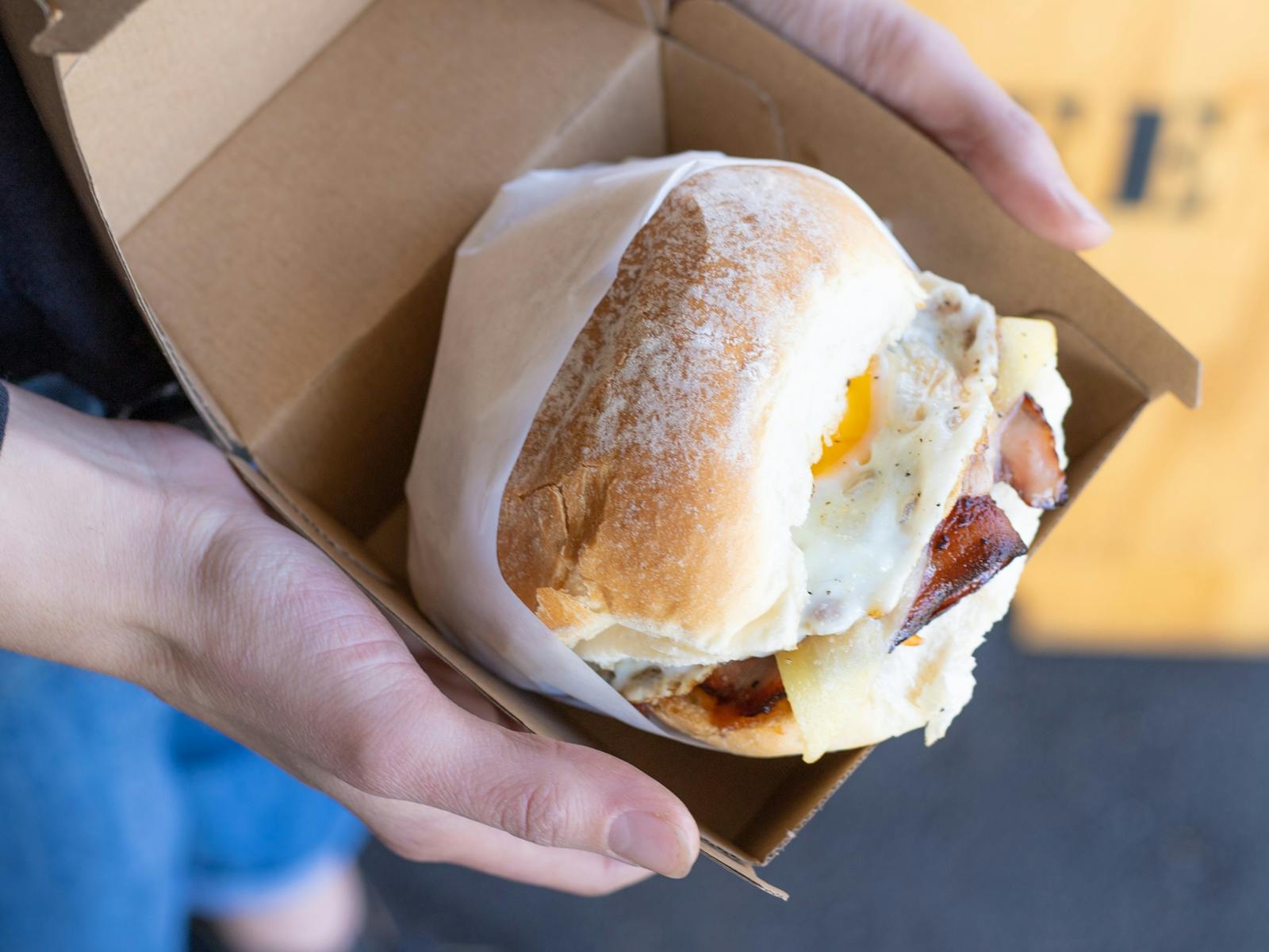 A small brown box held open with an egg and bacon soft bap roll inside