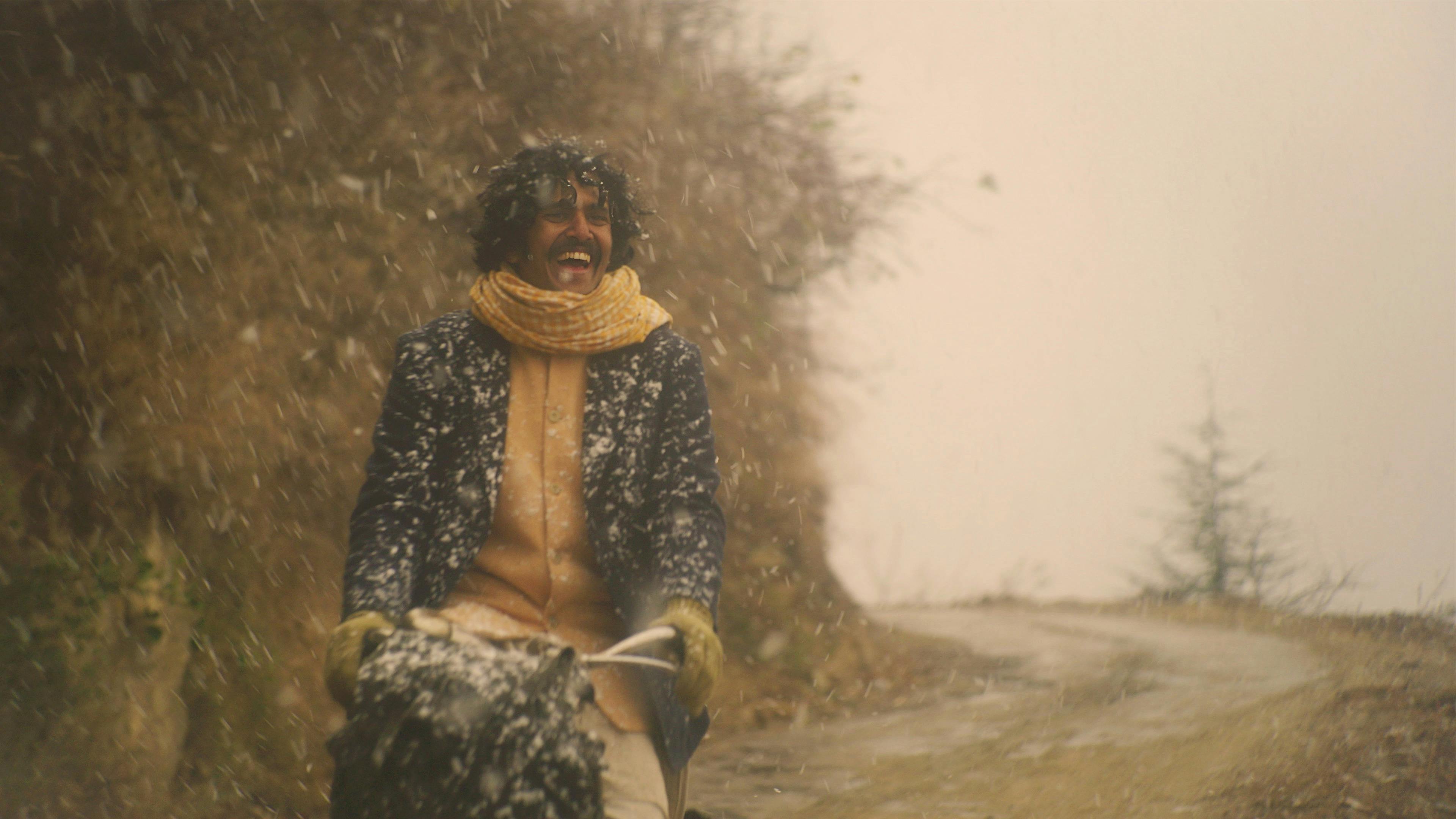 A smiling man, rides a bike through falling snow