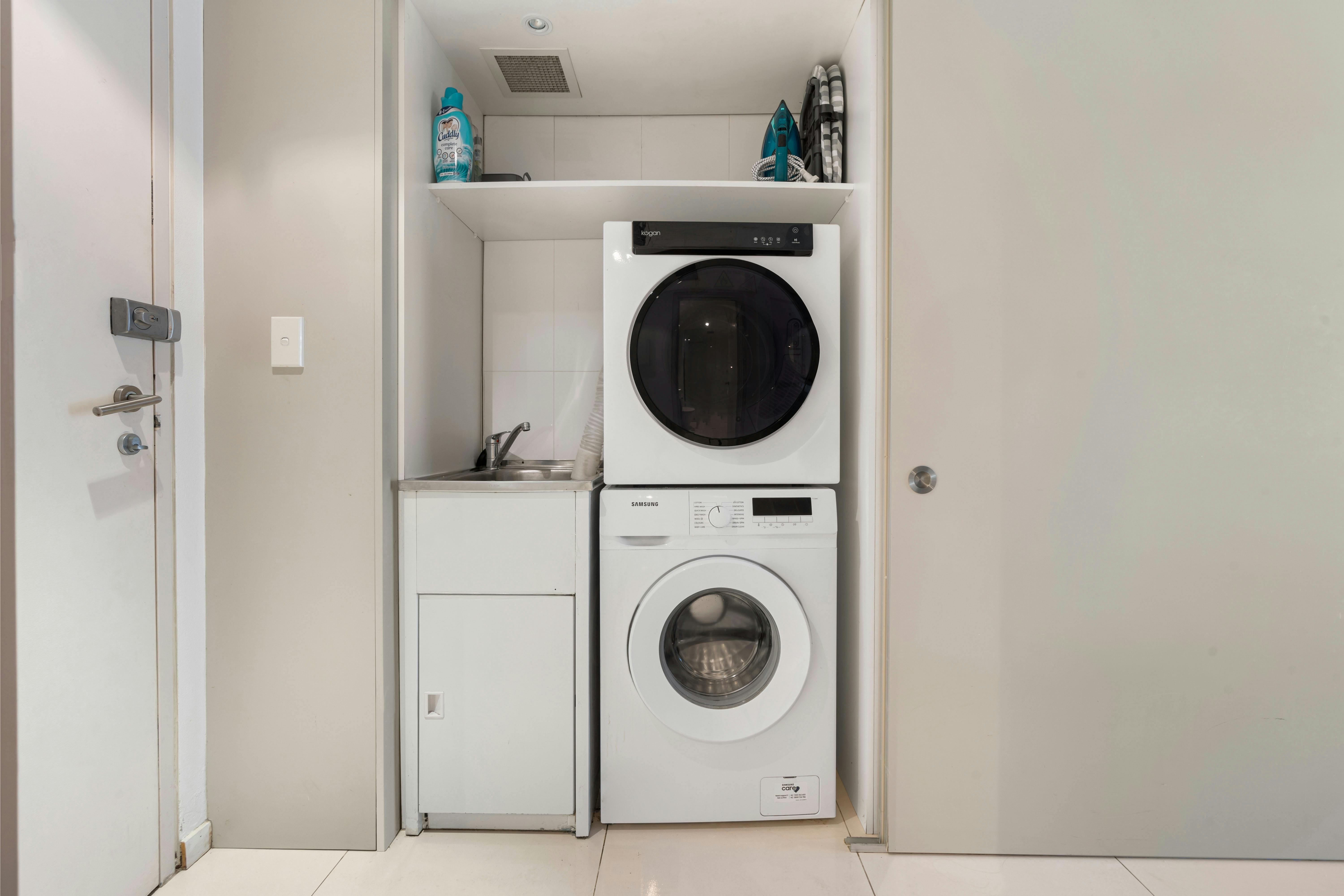 Modern laundry with stacked washer and dryer, sink, and storage shelves.