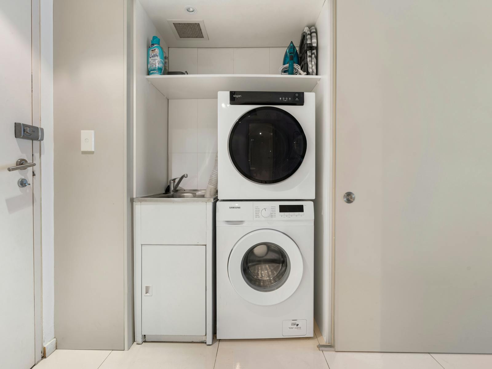 Modern laundry with stacked washer and dryer, sink, and storage shelves.